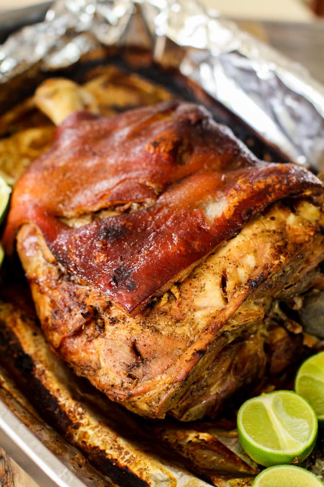 Cooked pork shoulder is on an aluminum foil lined pan with cut lime.