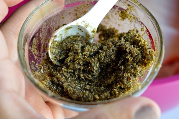 A glass bowl has a blend of fresh herbs in a paste.