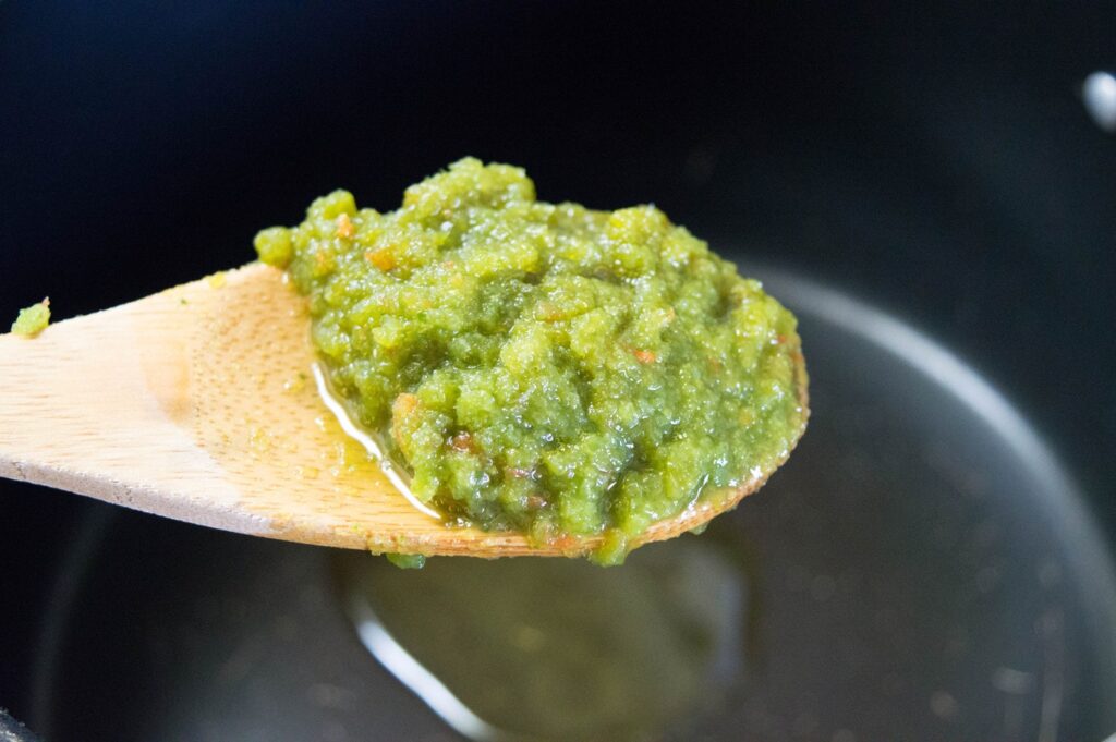 A wooden is spoon holding a green mixture of fresh sofrito.
