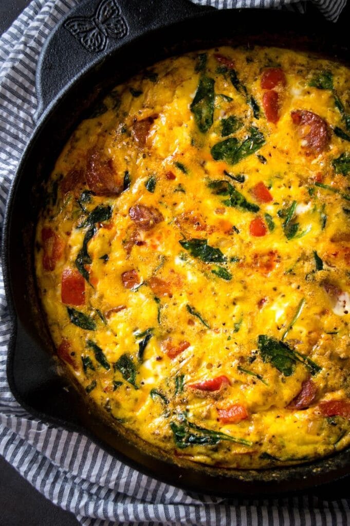 Cast iron pan filled with an egg bake filled with veggies with a black and white striped hand towel.