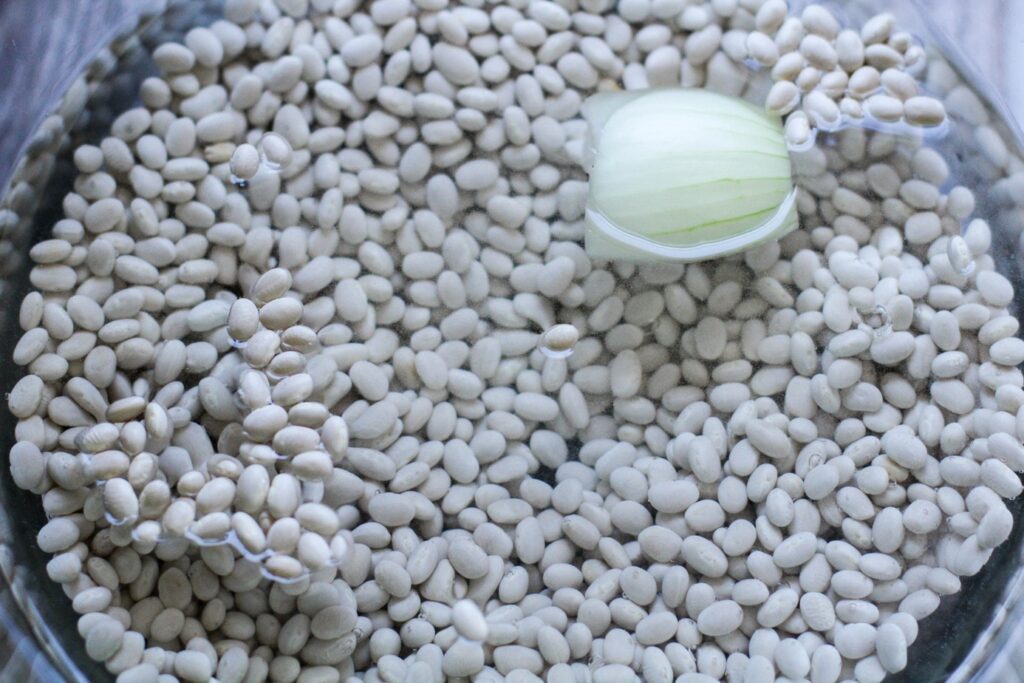 navy beans soaking in a bowl of water with a chunk of onion.