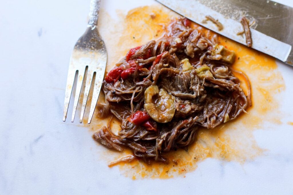 Ropa Vieja shredded on a cutting board with a fork and knife