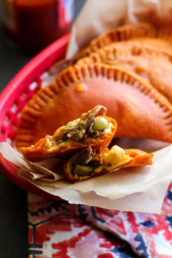 Empanada cut open in a red plastic basket with whole empanadas