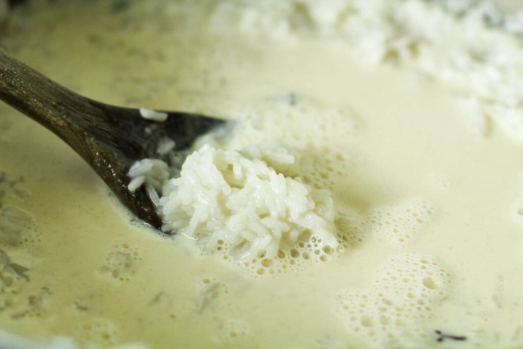 rice surrounded by milk in a pot with a wooden spoon