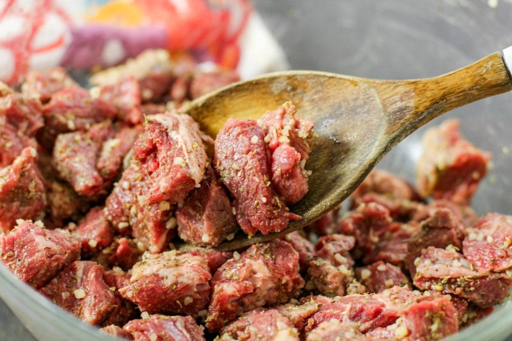 chopped steak that is seasoned on a wooden spoon