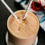 Papaya smoothie with straws inside with a colorful cloth behind it