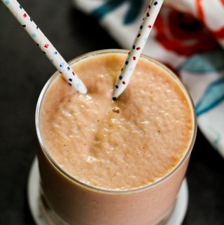 Papaya smoothie with straws inside with a colorful cloth behind it