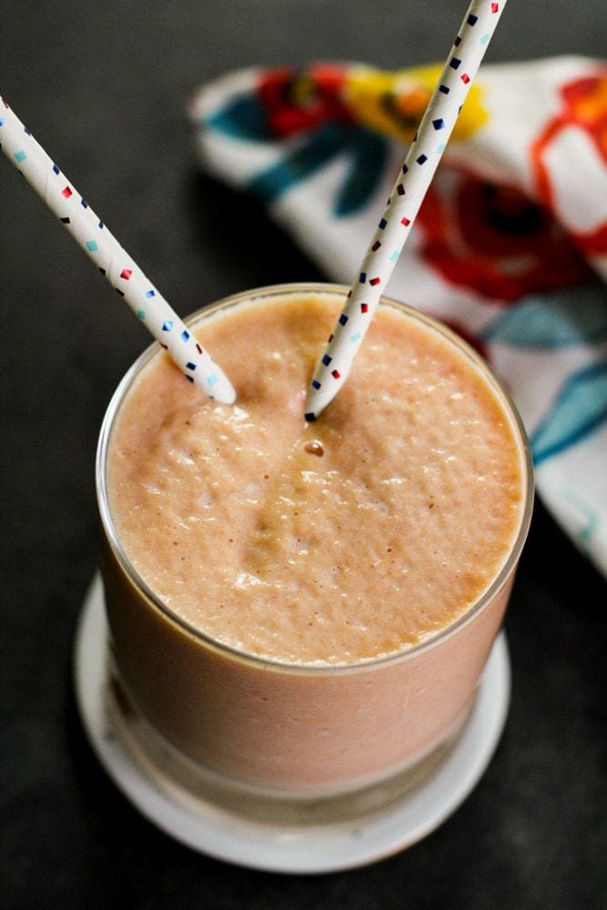 Papaya smoothie with straws inside with a colorful cloth behind it