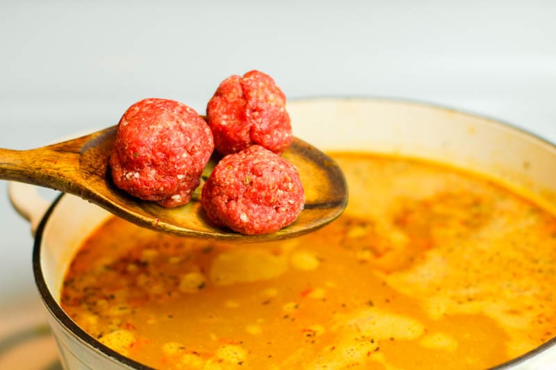 Raw albondigas on a spoon over the soup
