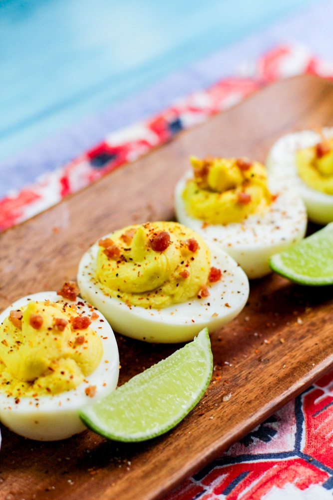 deviled eggs with bacon and tajin crumbled ona wooden platter with lime wedges nearby