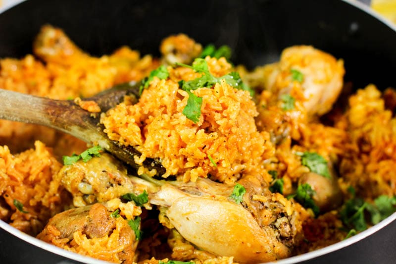 arroz con pollo in a black pan with a wooden spoon.