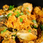 Cooked yellow rice in a pot with cooked drumsticks.