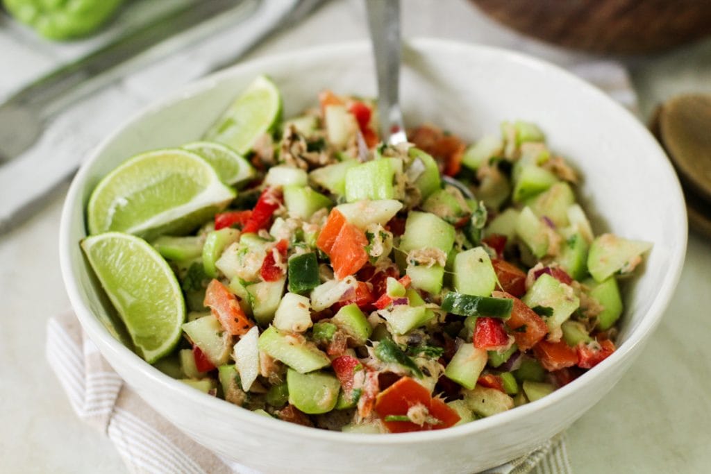 chayote tuna salad in a white bowl with lime wedges