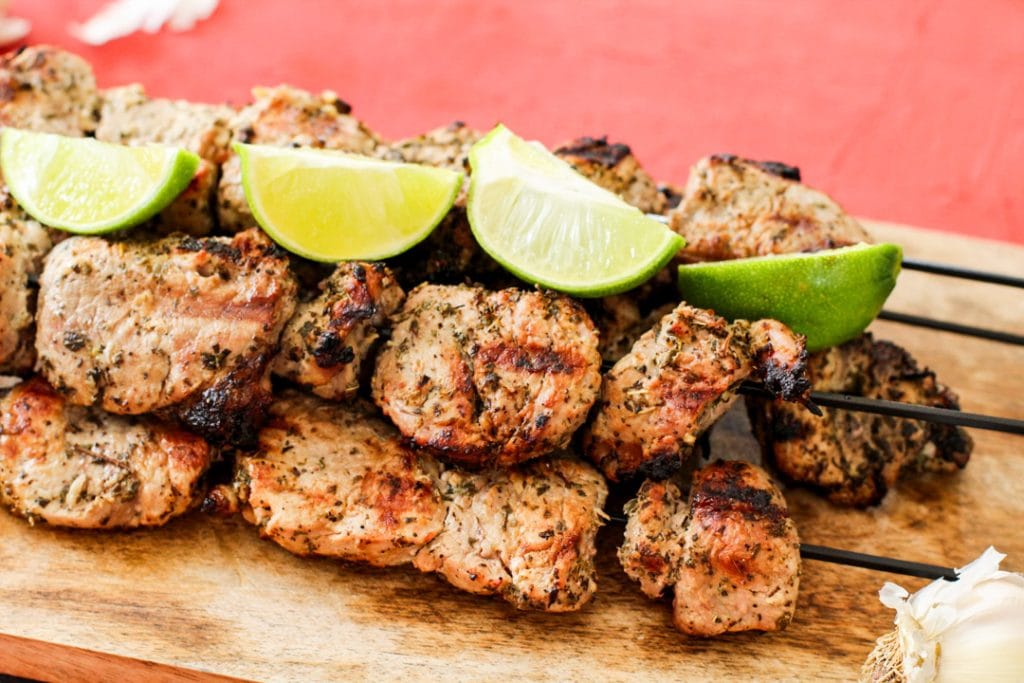 pork kabobs on a wooden platter with lime wedges