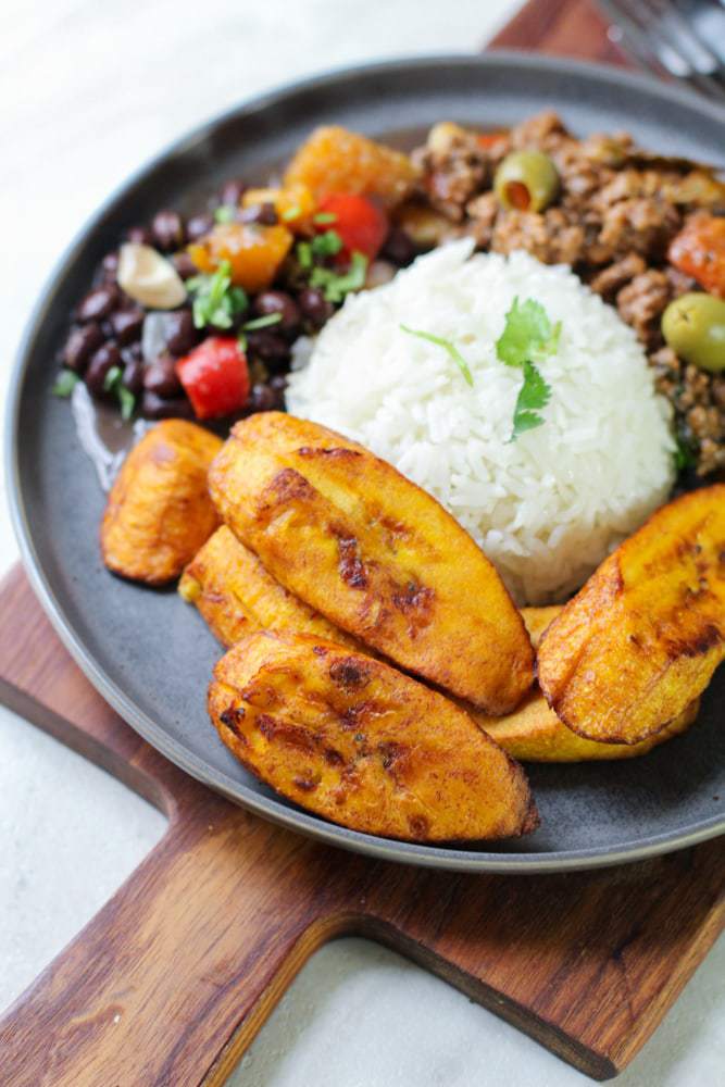 fried plantains on a gray plate with rice and beans