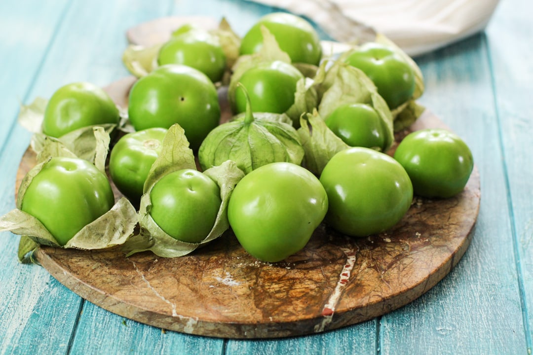 Fresh tomatillos are on a brown marble serving tray with a blue background