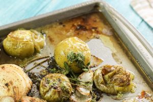 A metal sheet pan is full of roasted tomatillos, garlic, and cilantro with a blue background.