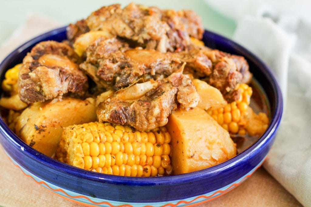 oxtails in a blue bowl with corn and potatoes
