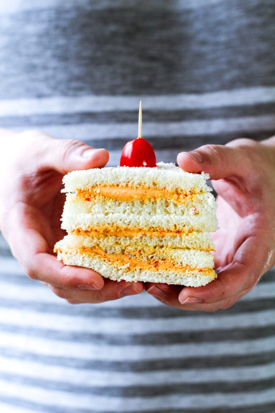 man holding 3 sliced sandwiches with a tomato in a toothpick