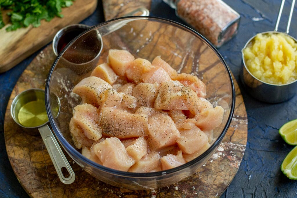 Raw chicken and salt, pepper, and corn oil in a glass bowl