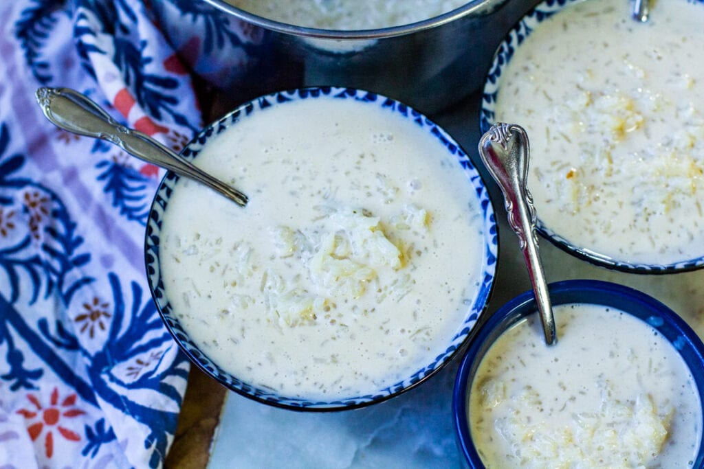 horizontal shot of multiple blue bowls filled with rice and milk with metal spoons