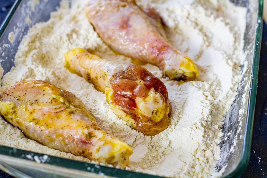 Seasoned chicken laying over flour mixture.