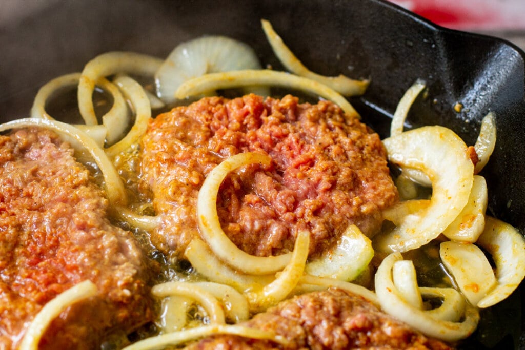 raw steak and onions cooking on a cast iron pan