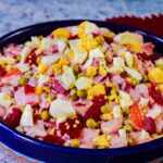 ensalada rusa in a blue bowl with eggs on top