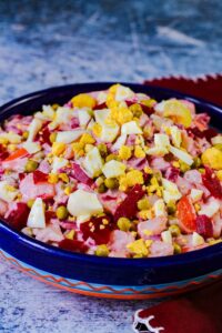 ensalada rusa in a blue bowl with eggs on top