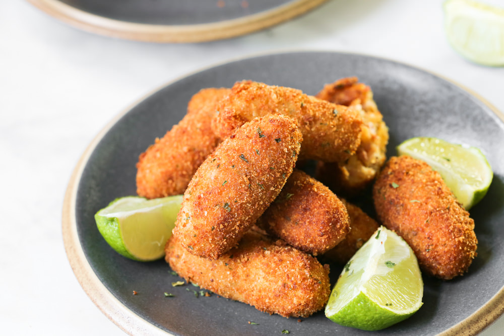 Whole fried croquettes on a gray plate with lime wedges.