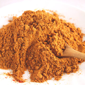 a pile of seasoning mix on a white plate with a wooden spoon