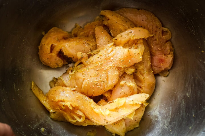 Raw chicken tender, seasoned with adobo in a metal bowl.