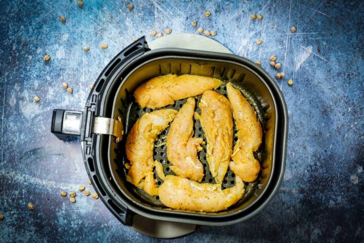 Raw chicken tenders lined on an air fryer.