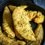 A pile of chicken tenders in a black cast iron pan.