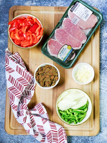 Pork and ingredients like bell pepper and onions on a wooden cutting board.