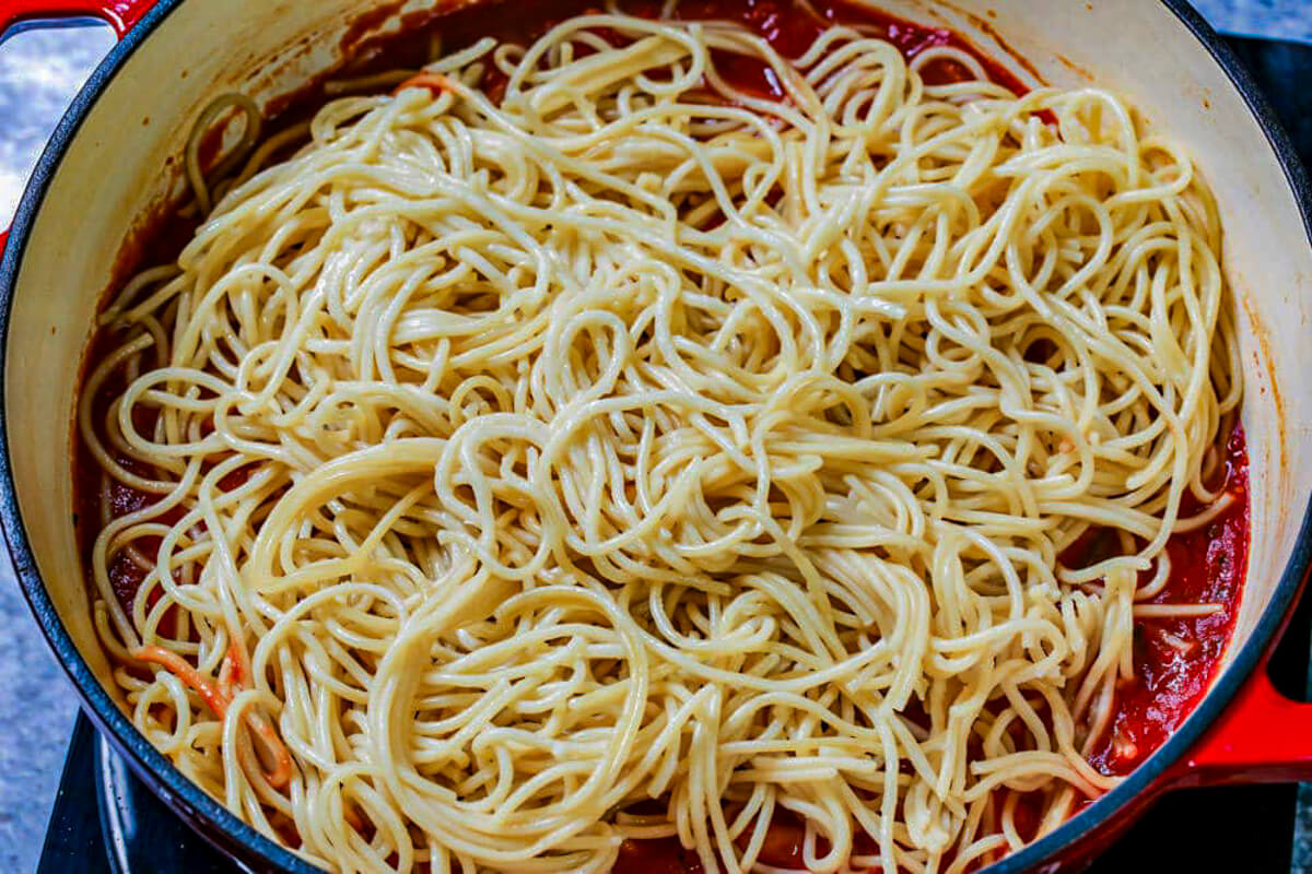 Cooked pasta tossed into spaghetti with pork chop sauce in a pot.
