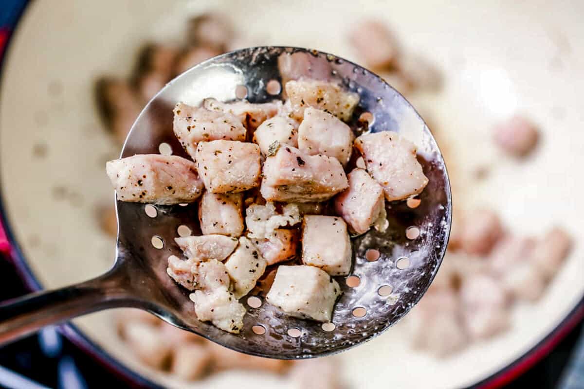 Removing pork chops from the pot with a metal spoon.