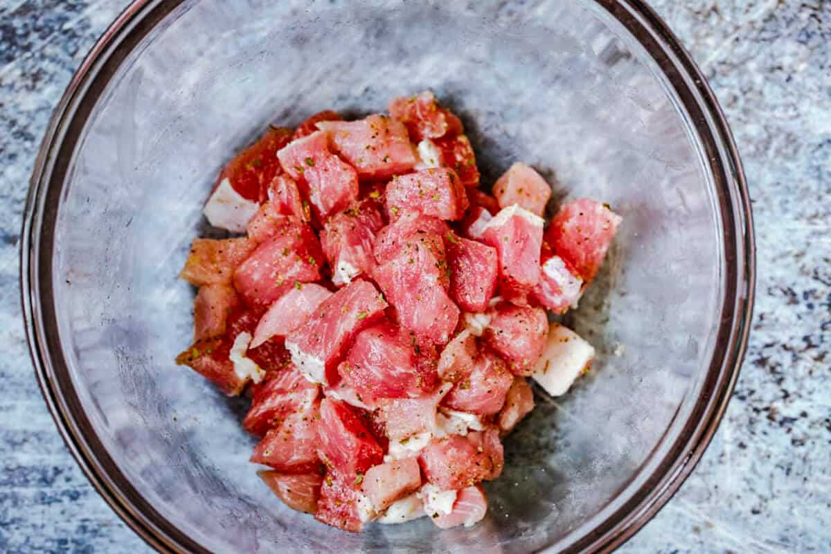 Seasoned raw cut pork in glass bowl.