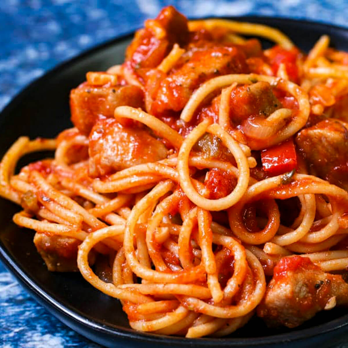 Close up shot of spaghetti with pork chops on a black plate with a blue background.