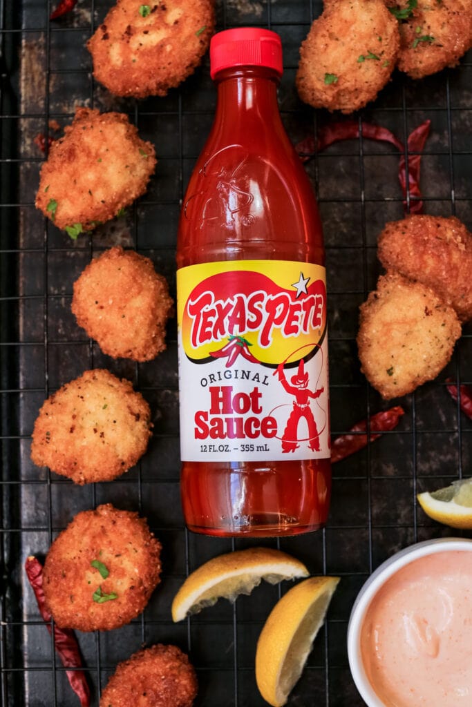 bottle of hot sauce surrounded by malanga frituras on a black pan