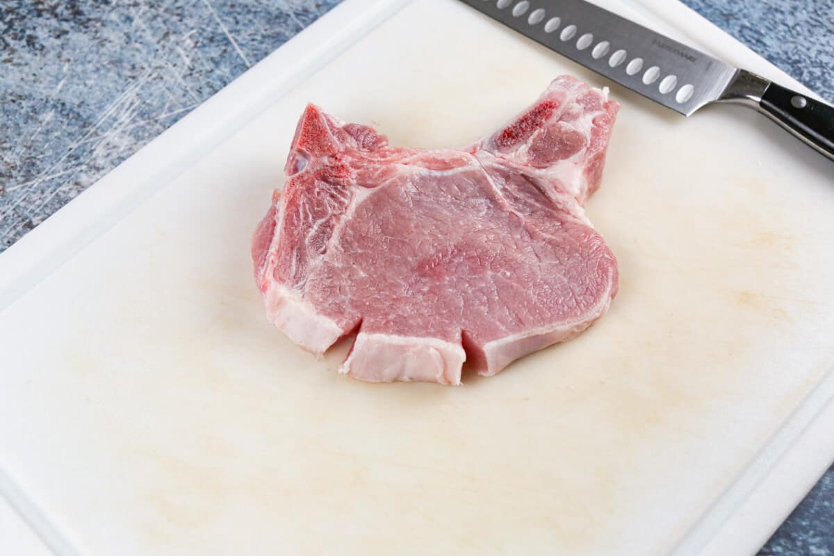 Raw pork chops with fat slit every 2 inches to keep from curling.