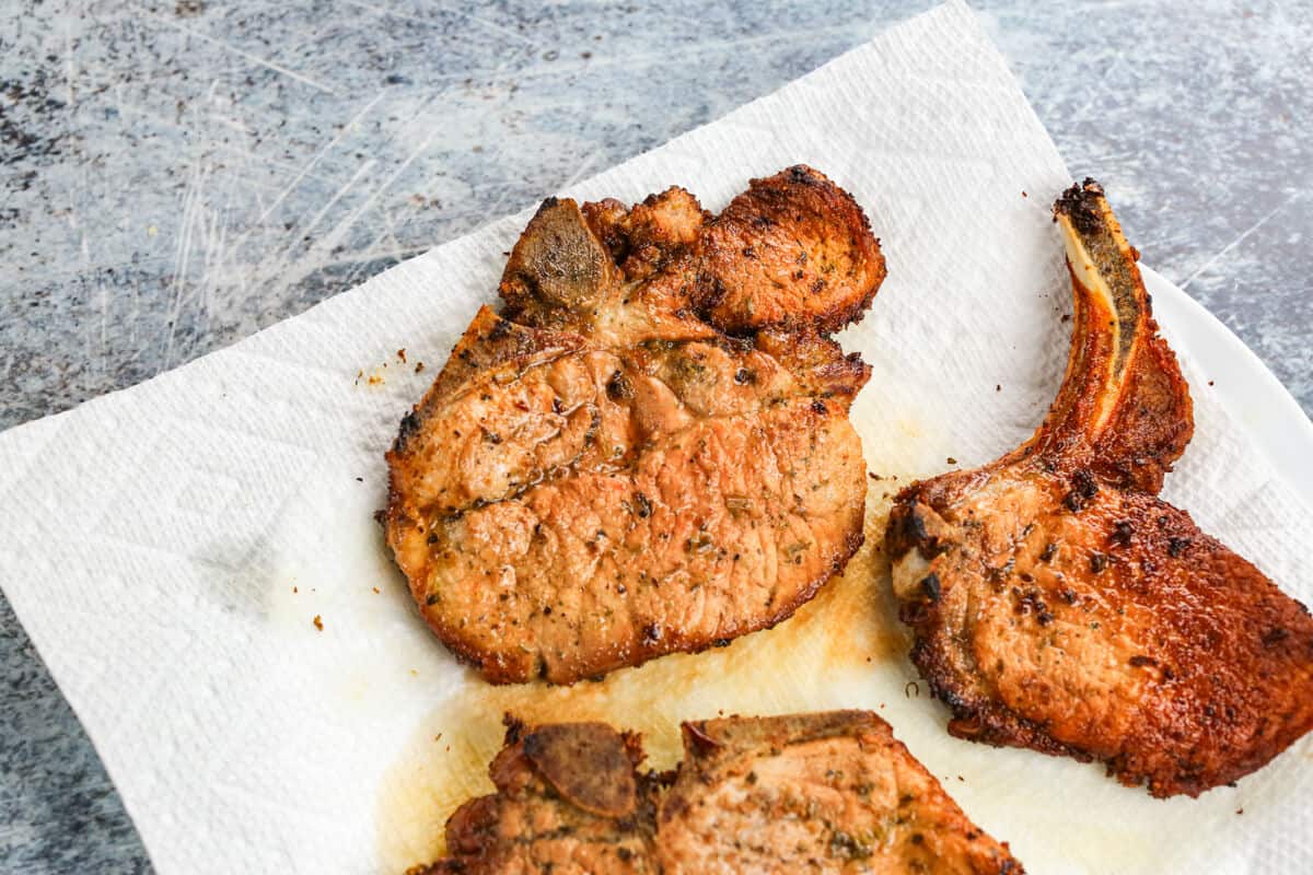 Freshly fried pork chops are draining on a paper towel lined plate to absorb excess oil.