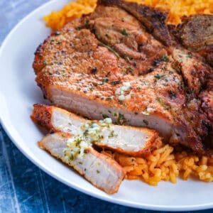 A crispy fried pork chop that is sliced is laying over a bed of Puerto Rican rice on a white plate.
