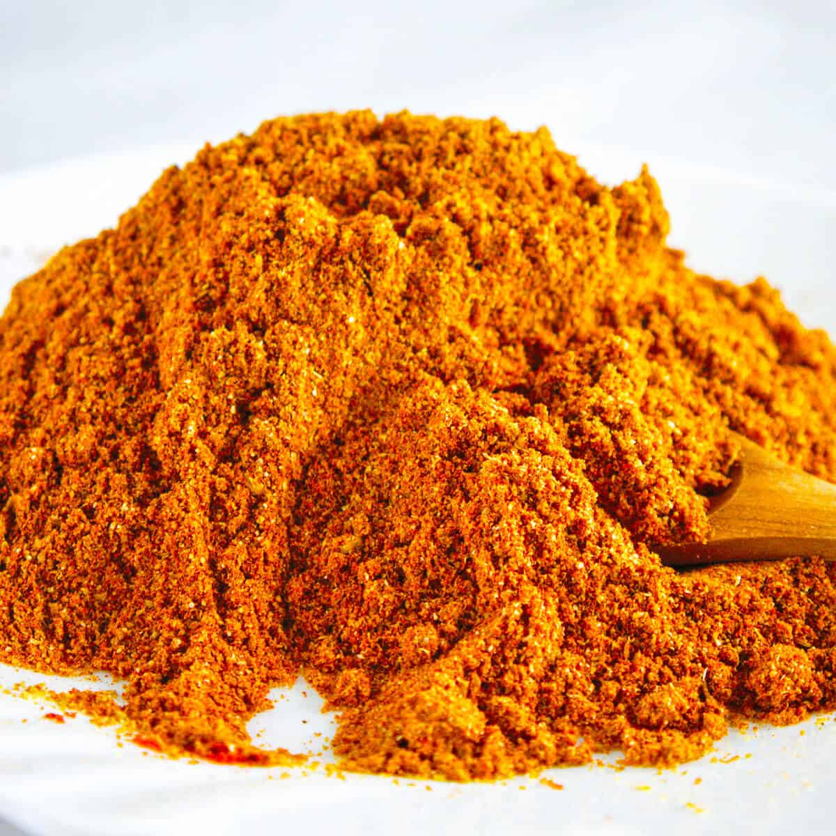 a small pile of orange seasoning with a small wooden spoon