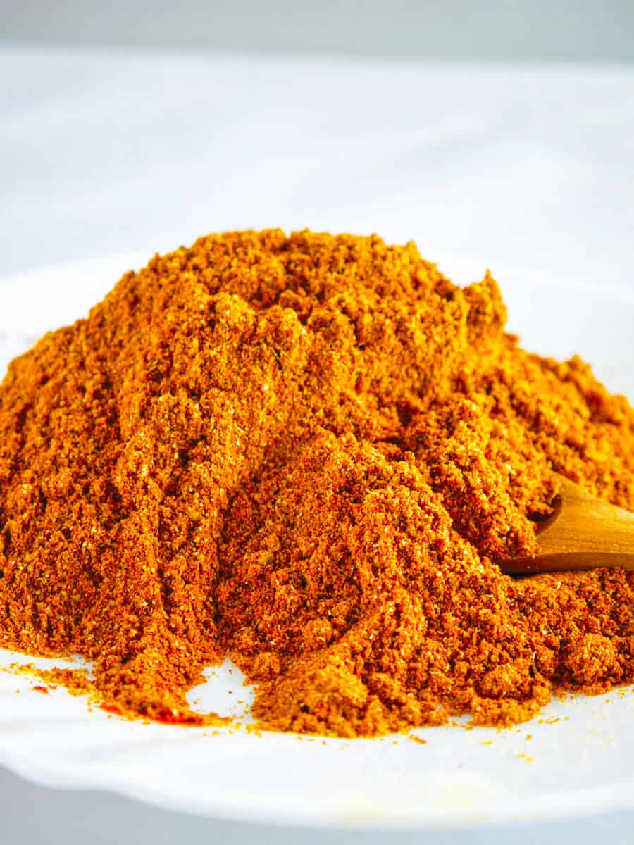 A large  pile of orange seasoning on a white background with a wooden spoon.