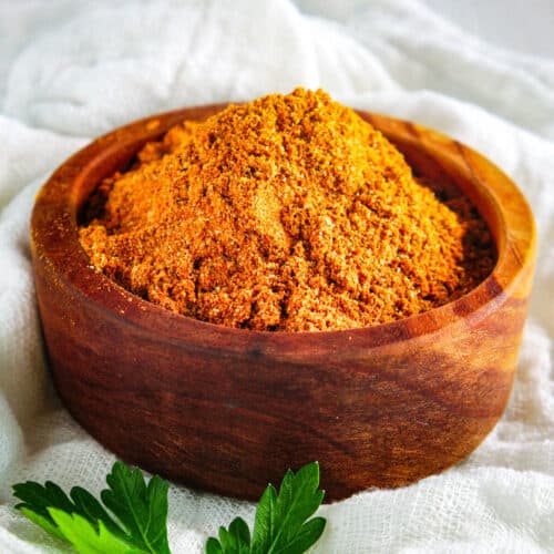 A wooden bowl full of orange sazon seasoning.