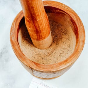 A wooden mortar and pestle filled with dry adobo seasoning.