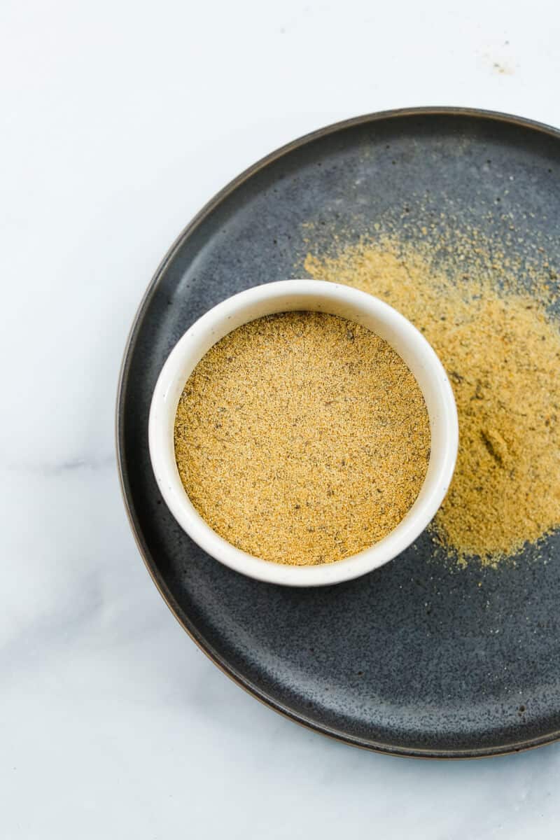 A white bowl filled with an all-purpose seasoning blend over a gray plate.