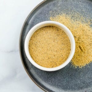 A small white ramekin filled with adobo seasoning over a gray plate.
