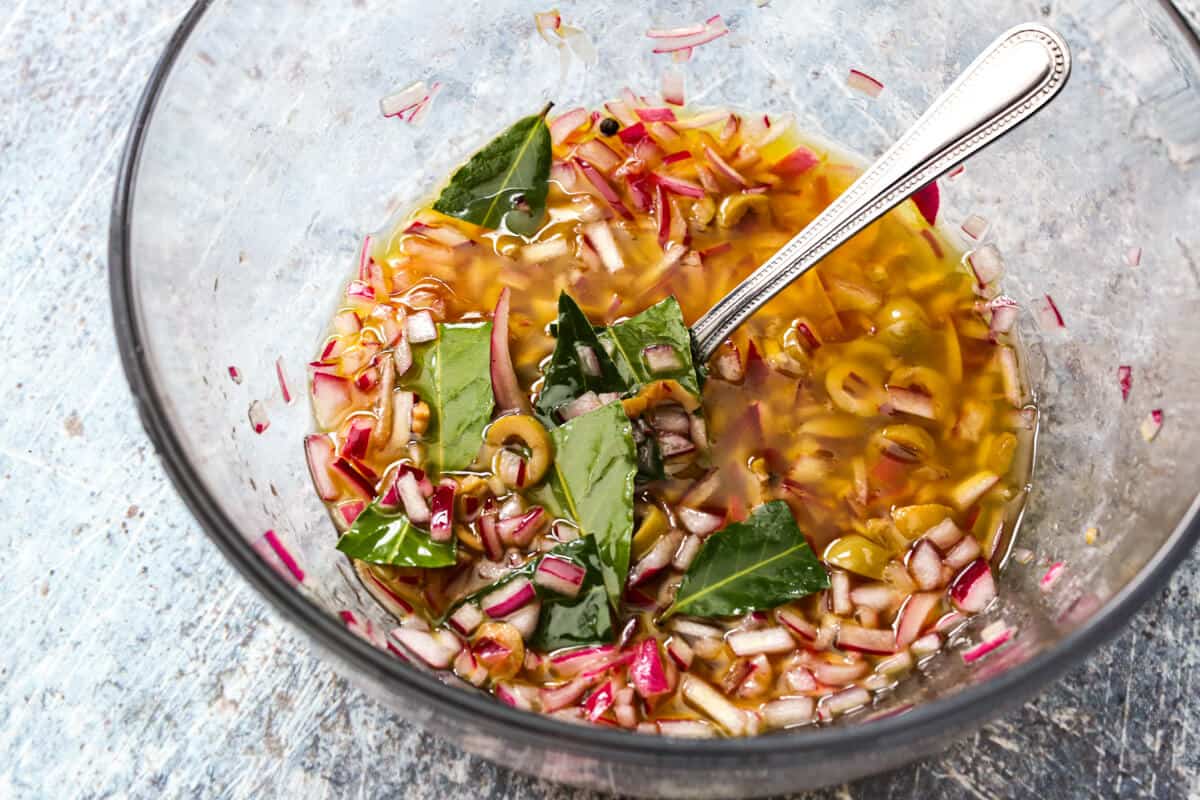 Pickled onions, olives, and bay leaves in a glass bowl.